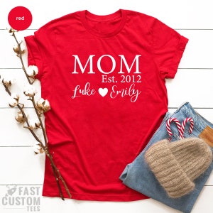 May include: Red t-shirt with white text that reads "MOM Est. 2012 Luke Emily" with a heart symbol between the names.