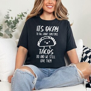 May include: A black t-shirt with white text that reads "It's okay to fall apart sometimes. Tacos do and we still love them." The shirt features a cartoon taco with a smiling face.