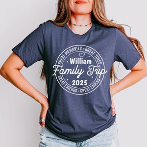 May include: A navy blue short-sleeve t-shirt featuring a white circular graphic with the text "William Family Trip 2025" in the center, surrounded by the phrases "Great Memories," "Great Times," "Great Friends," and "Great Laughs" with a heart.