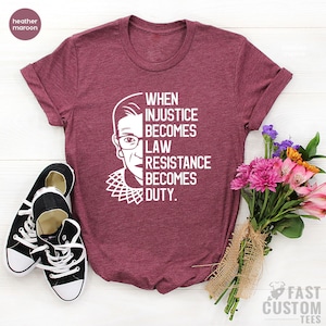 May include: A heather maroon t-shirt with a white graphic of Ruth Bader Ginsburg and the text "When injustice becomes law resistance becomes duty."
