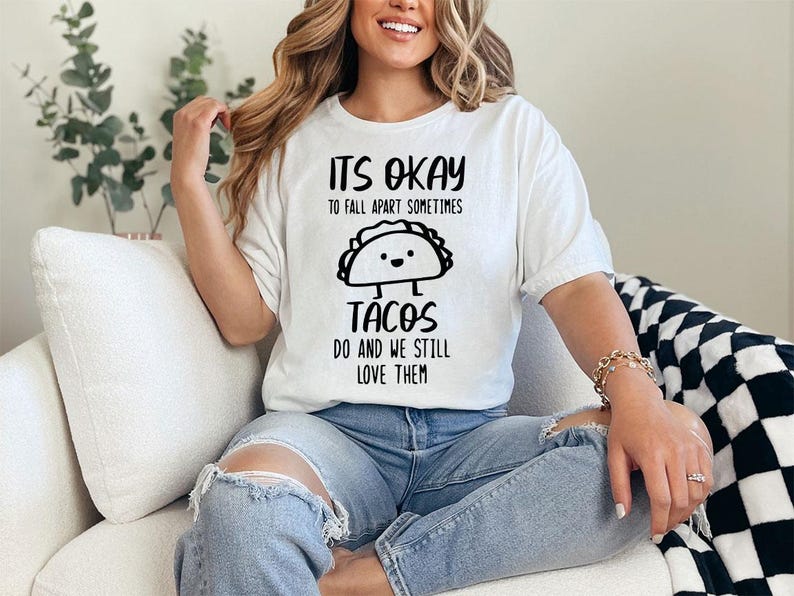 May include: White t-shirt with a black graphic that says "It's okay to fall apart sometimes tacos do and we still love them". The graphic features a cartoon taco with a smiling face.