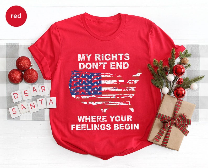 May include: A red t-shirt featuring the text "MY RIGHTS DON'T END WHERE YOUR FEELINGS BEGIN" and an American flag design in the shape of the United States. The shirt is shown with festive Christmas decorations.