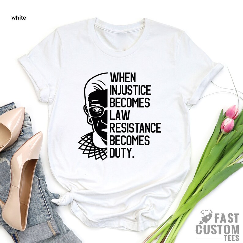 May include: White t-shirt with a black and white illustration of Ruth Bader Ginsburg and the text "When injustice becomes law, resistance becomes duty."