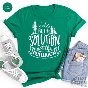 May include: A kelly green t-shirt with white text that reads "Be the Solution not the Pollution". The text is surrounded by a stylized banner and two small pine trees.