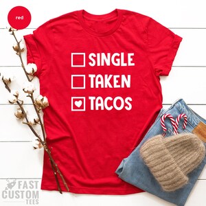 May include: Red t-shirt with white text that reads "SINGLE TAKEN TACOS" with a heart replacing the "O" in tacos.