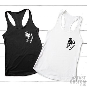 May include: Two racerback tank tops with a pug graphic on the front. The tank top on the left is black and the tank top on the right is white.