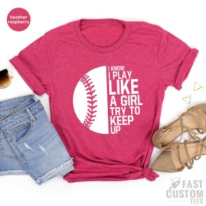 Op de afbeelding: Een heather framboos t-shirt met een witte baseball afbeelding en de tekst "I know I play like a girl try to keep up".