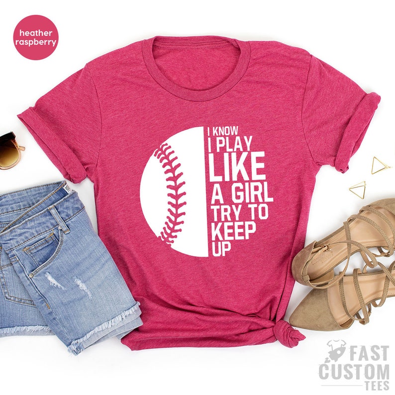 Op de afbeelding: Een heather framboos t-shirt met een witte baseball afbeelding en de tekst "I know I play like a girl try to keep up".