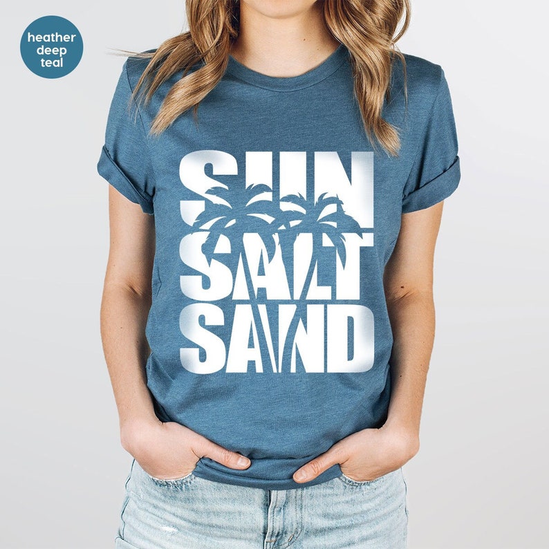 May include: A heather deep teal t-shirt with a white graphic design that says "SUN SALT SAND" with palm trees incorporated into the design.