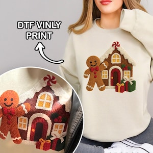 A woman wearing a white sweater with a detailed embroidered design of a gingerbread house and two gingerbread men.