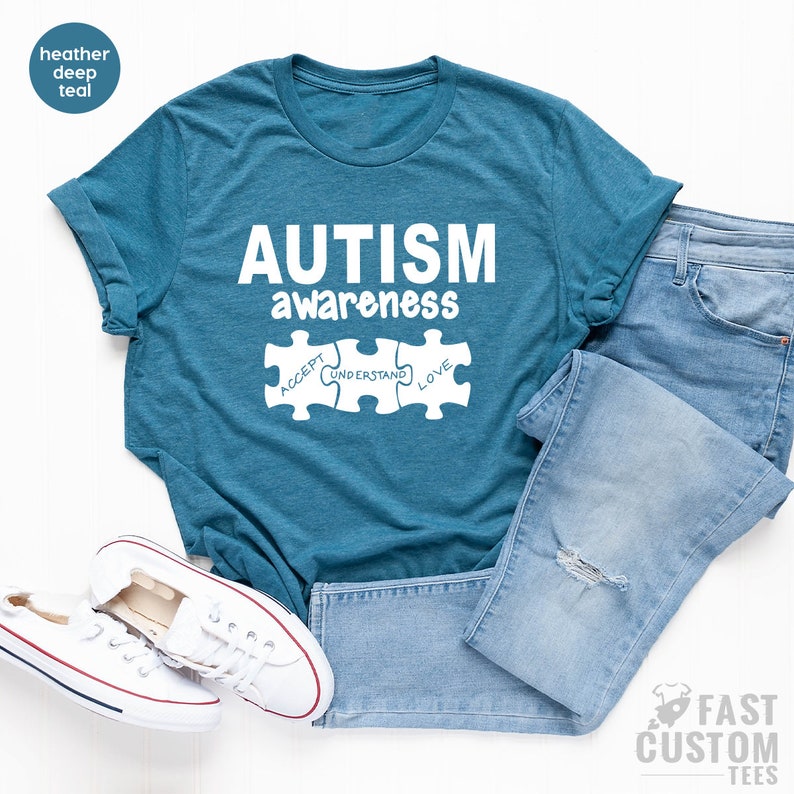 May include: A teal blue t-shirt with the text "AUTISM awareness" and three puzzle pieces that say "ACCEPT", "UNDERSTAND", and "LOVE".