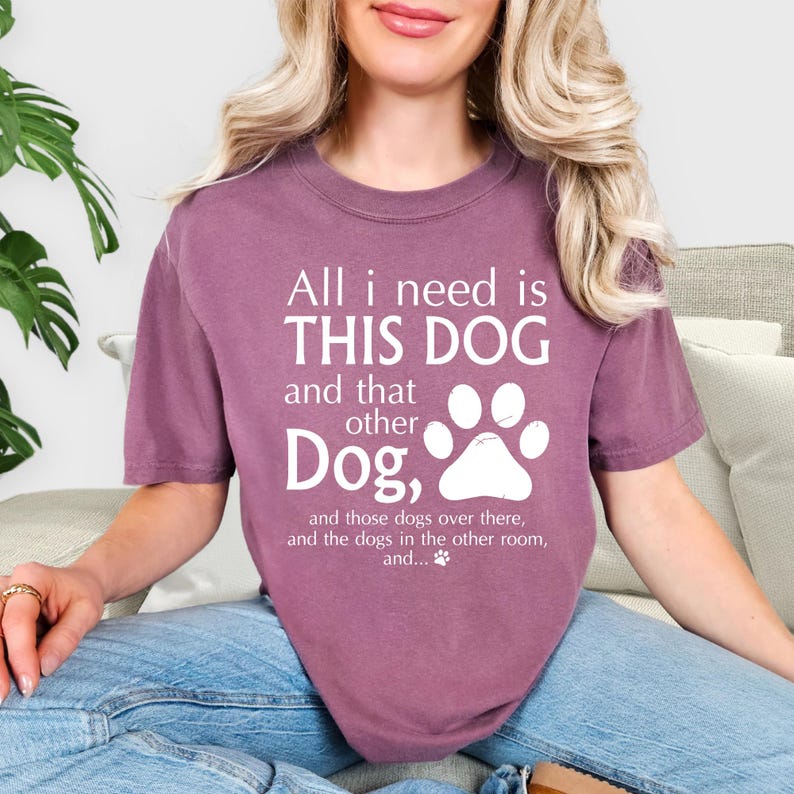 A woman wearing a purple t-shirt with a humorous text printed on it, sitting on a couch.