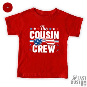 May include: Red t-shirt with a white graphic that says "The Cousin Crew" with an American flag design in sunglasses.