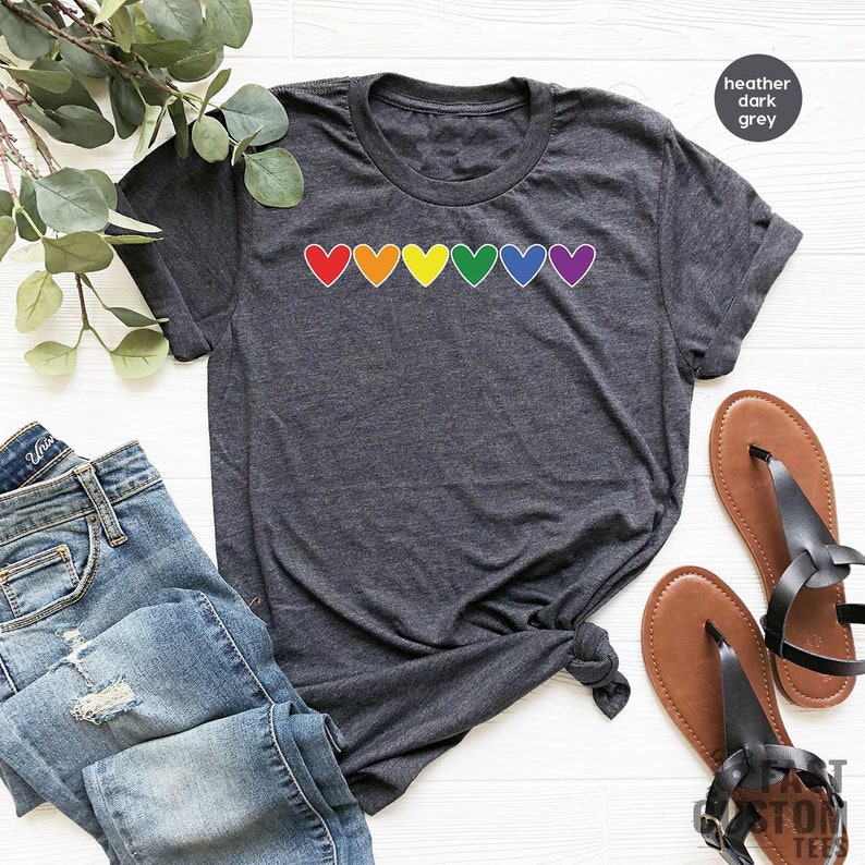 May include: A heather dark grey t-shirt with a row of rainbow coloured hearts across the chest.
