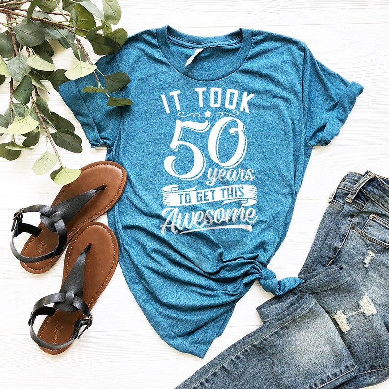 May include: A teal blue t-shirt with white text that reads "It took 50 years to get this awesome".