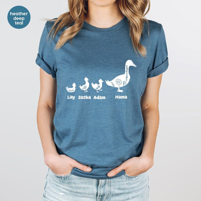 Puede incluir: Una camiseta de color azul oscuro con un gr&aacute;fico blanco de una l&iacute;nea de patos. Los patos est&aacute;n etiquetados como "Lily", "Sasha", "Adam" y "Mama".