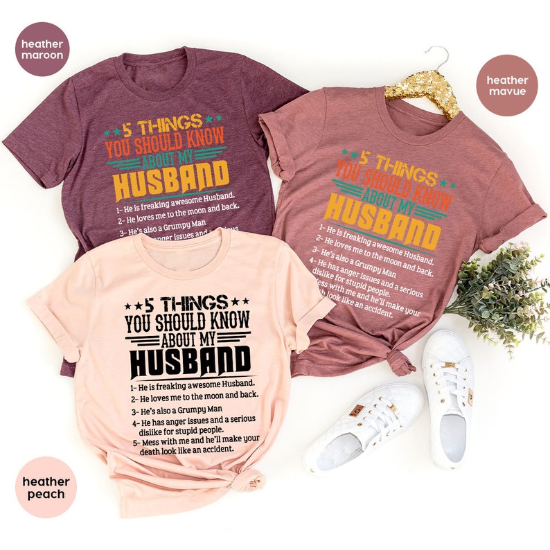 May include: Three t-shirts with a humorous design featuring a list of five things to know about a husband. The shirts are in heather maroon, heather peach, and heather mauve. The text on the shirts reads "5 Things You Should Know About My Husband".