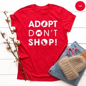 May include: Red t-shirt with white text that reads "Adopt Don't Shop!" with a silhouette of a cat and dog in circles.
