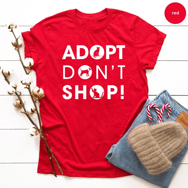 May include: Red t-shirt with white text that reads "Adopt Don't Shop!" with a silhouette of a cat and dog in circles.
