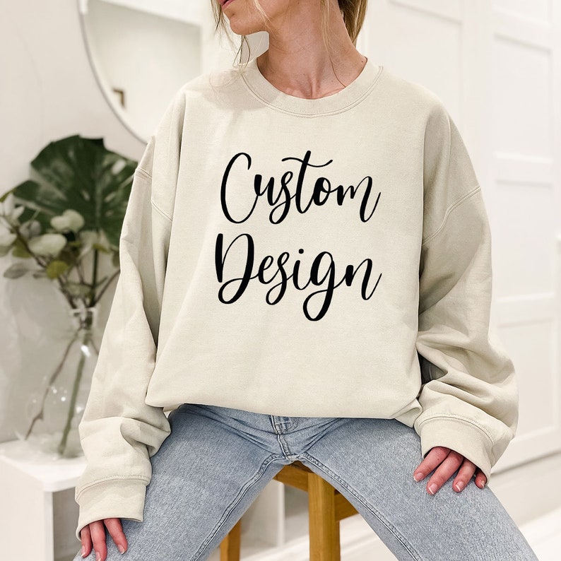 May include: A beige sweatshirt with the text "Custom Design" printed in black on the front.
