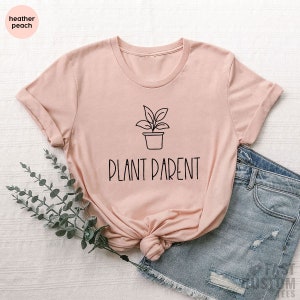 May include: A light pink t-shirt with a black line drawing of a potted plant and the text "PLANT PARENT" in black.