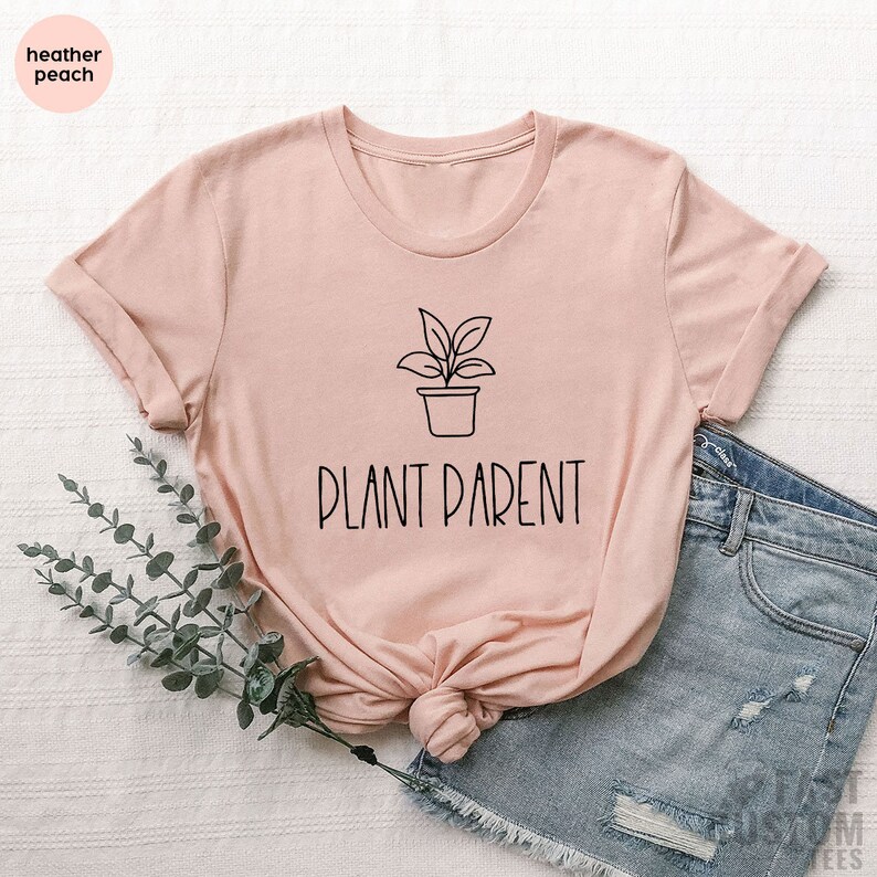 May include: A light pink t-shirt with a black line drawing of a potted plant and the text "PLANT PARENT" in black.