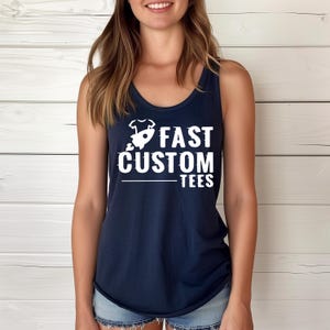 May include: A navy blue tank top with the words "FAST CUSTOM TEES" in large white letters. The text is accompanied by a small graphic. The tank top is sleeveless and has a scoop neck.