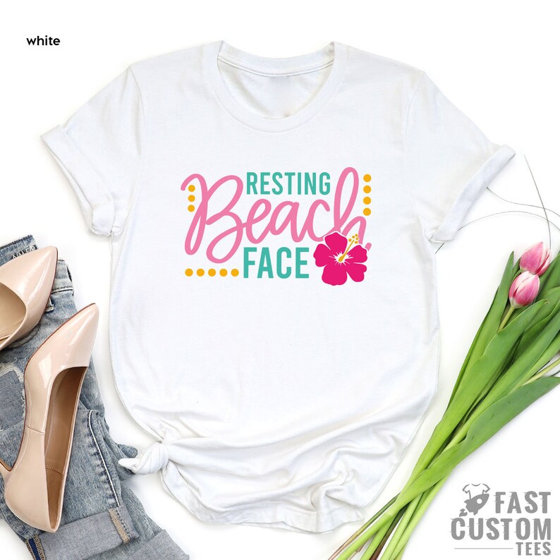 May include: White t-shirt with the text "Resting Beach Face" in teal and pink lettering with a pink hibiscus flower.