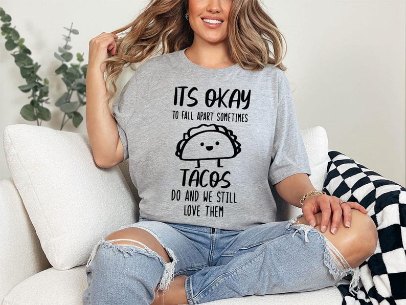 May include: A gray t-shirt with black text that reads "It's okay to fall apart sometimes tacos do and we still love them". The shirt features a cartoon taco with a smiling face.