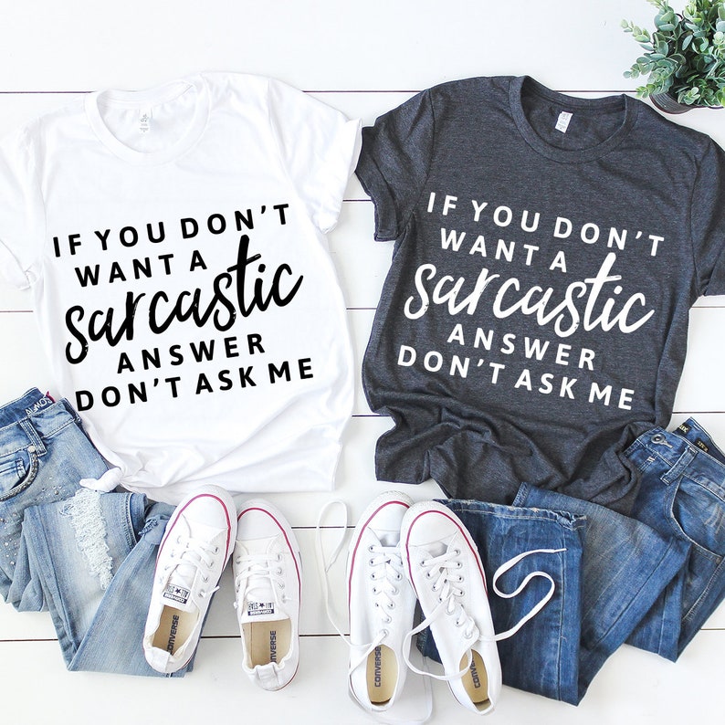 May include: Two t-shirts with a humorous saying. The white t-shirt says "If you don't want a sarcastic answer don't ask me". The gray t-shirt says "If you don't want a sarcastic answer don't ask me".