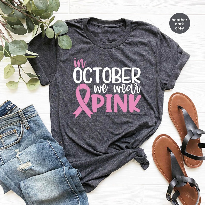 Pu&ograve; includere: Una maglietta color grigio scuro melange con il testo "in OCTOBER we wear PINK" e una grafica a nastro rosa.