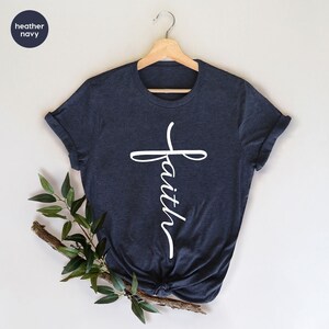May include: A heather navy blue t-shirt with a white cross and the word "faith" written vertically on it.