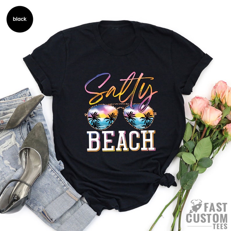 May include: Black t-shirt with a graphic of sunglasses with a sunset and palm trees reflection. The text "Salty Beach" is written in a colorful font.