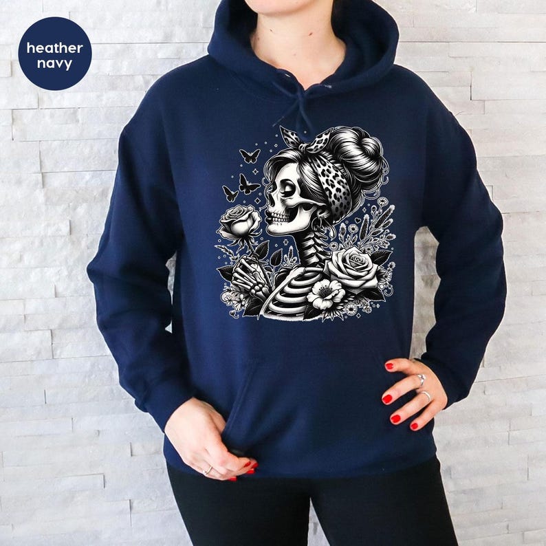 Puede incluir: Una sudadera con capucha azul marino con un gr&aacute;fico blanco de una mujer esqueleto sosteniendo una rosa, rodeada de mariposas y flores.