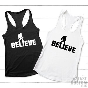 May include: Two black and white tank tops with a silhouette of Bigfoot walking and the word "BELIEVE" printed on them.