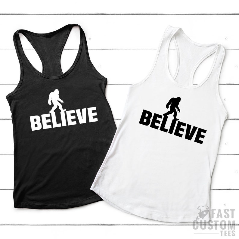 May include: Two black and white tank tops with a silhouette of Bigfoot walking and the word "BELIEVE" printed on them.