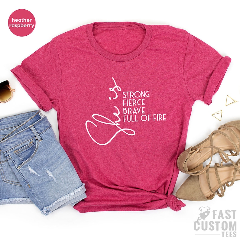 Pode incluir: Camiseta heather framboesa com texto branco que diz "She is strong, fierce, brave, full of fire".