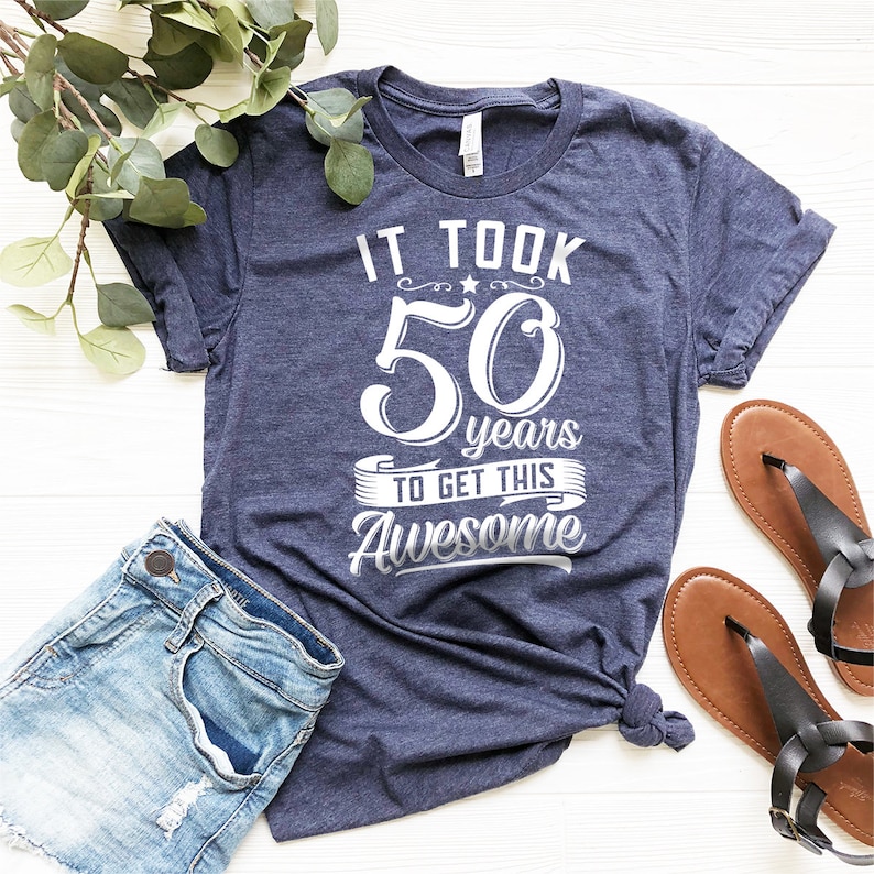May include: A navy blue t-shirt with white text that reads "It took 50 years to get this Awesome".