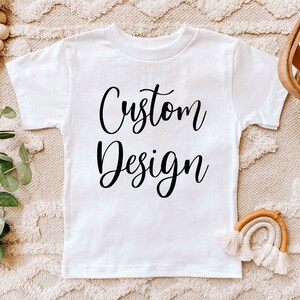 May include: White t-shirt with the text "Custom Design" printed in black cursive font.