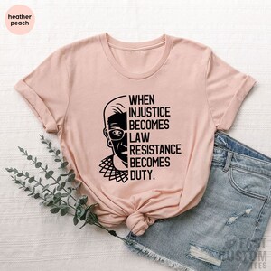 May include: A light pink t-shirt with a black and white image of Ruth Bader Ginsburg and the text "When injustice becomes law, resistance becomes duty."