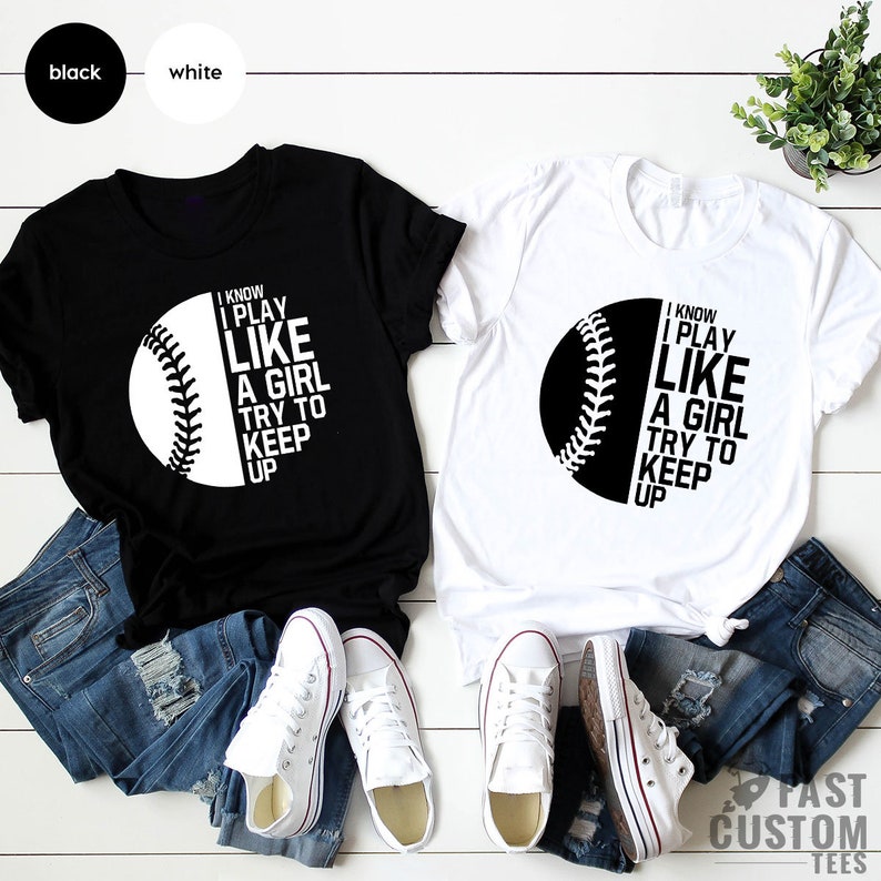 Op de afbeelding: Twee T-shirts met een baseball-afbeelding en de tekst "I know I play like a girl try to keep up". Een T-shirt is zwart met witte tekst en de andere is wit met zwarte tekst.