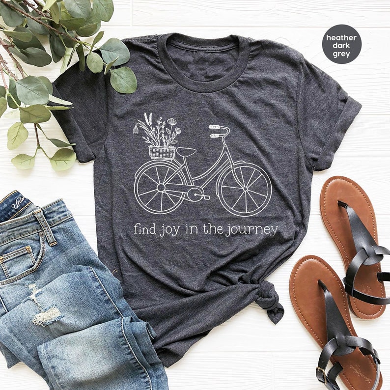 May include: A heather dark grey t-shirt with a white graphic of a bicycle with flowers in a basket. The text "find joy in the journey" is printed below the bicycle.