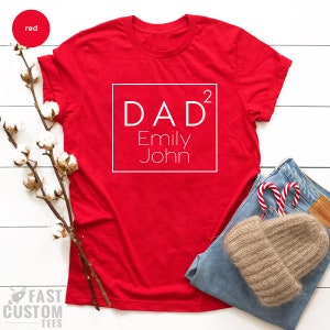 May include: Red t-shirt with a white square that says "DAD&sup2; Emily John" on it.