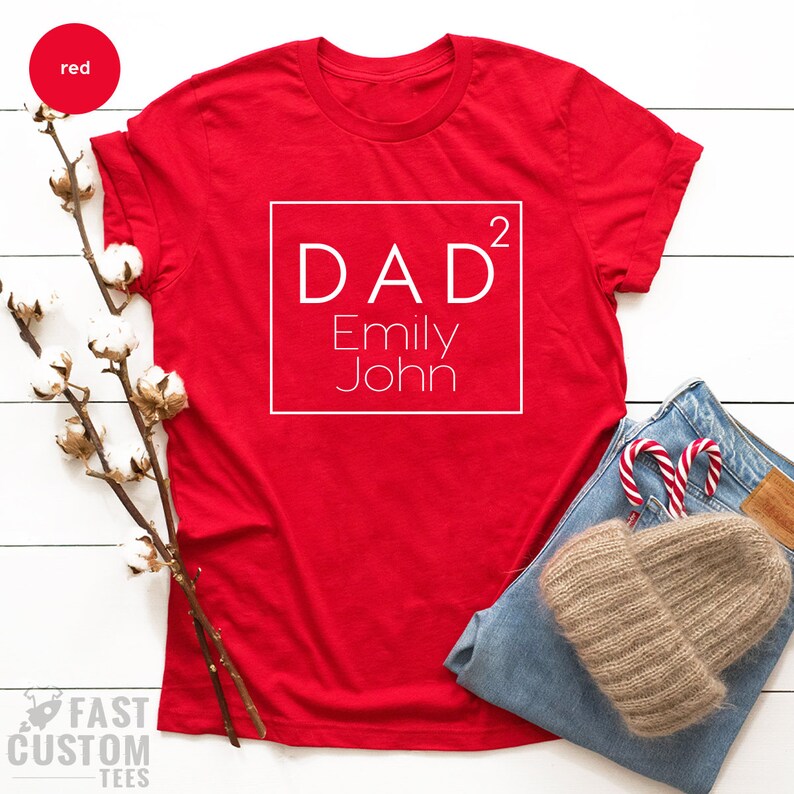May include: Red t-shirt with a white square that says "DAD&sup2; Emily John" on it.