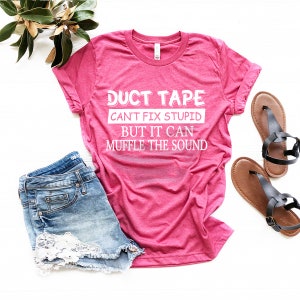 May include: A pink t-shirt with the text "DUCT TAPE CAN'T FIX STUPID BUT IT CAN MUFFLE THE SOUND" in white. The shirt is paired with denim shorts and brown sandals.