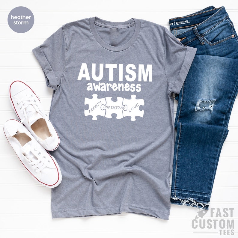 May include: A heather storm grey t-shirt with the text "AUTISM awareness" and three puzzle pieces that say "ACCEPT", "UNDERSTAND", and "LOVE".