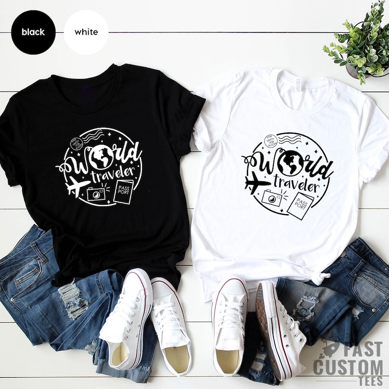 May include: Two t-shirts, one black and one white, with a graphic design of a globe, airplane, camera, and passport with the text "World Traveler".