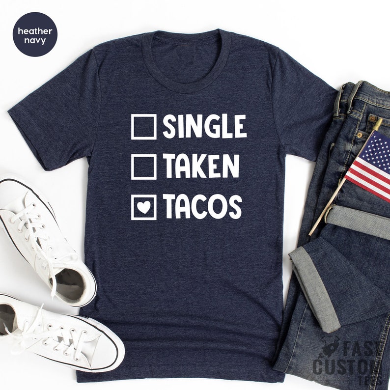 May include: A heather navy blue t-shirt with a white graphic that reads "Single, Taken, Tacos" with a heart replacing the checkmark for the "Tacos" option.