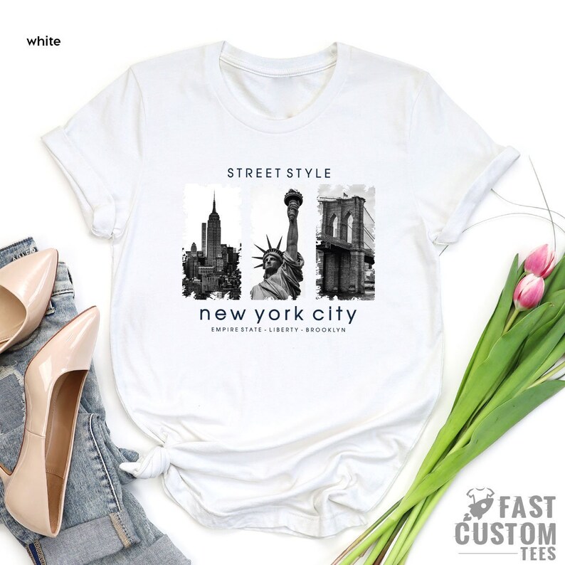 May include: White t-shirt with a black and white graphic print of the New York City skyline, the Statue of Liberty, and the Brooklyn Bridge. The text "STREET STYLE" and "new york city" is printed on the shirt.