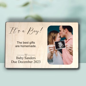 May include: A wooden sign with the text "It's a Boy! The best gifts are homemade. Baby Sanders Due December 2023" and a photo of a couple holding an ultrasound image.